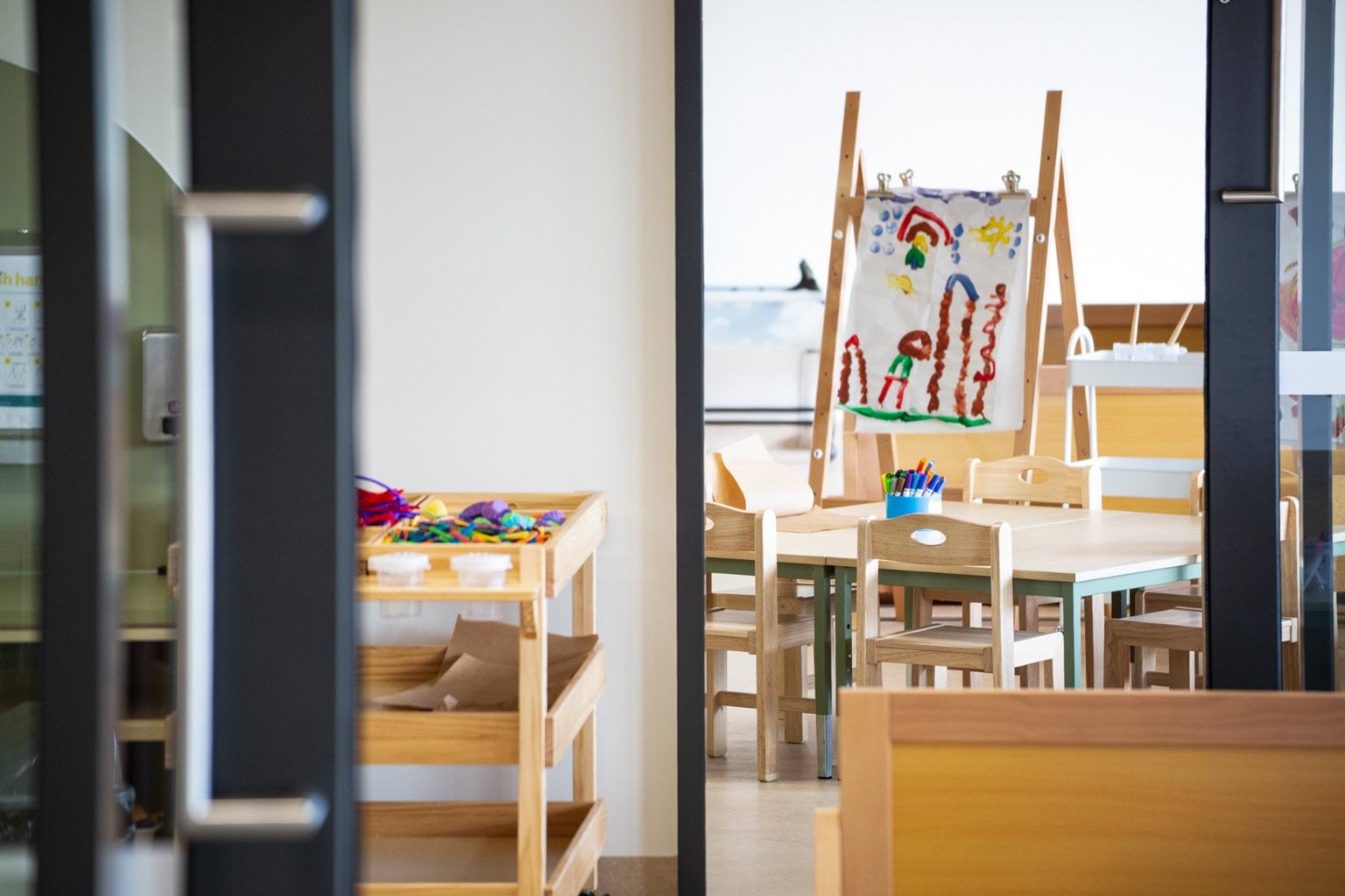 View into room with tables and easel showing children’s paintings at Early Learning Victoria Wimbi (Fawkner).