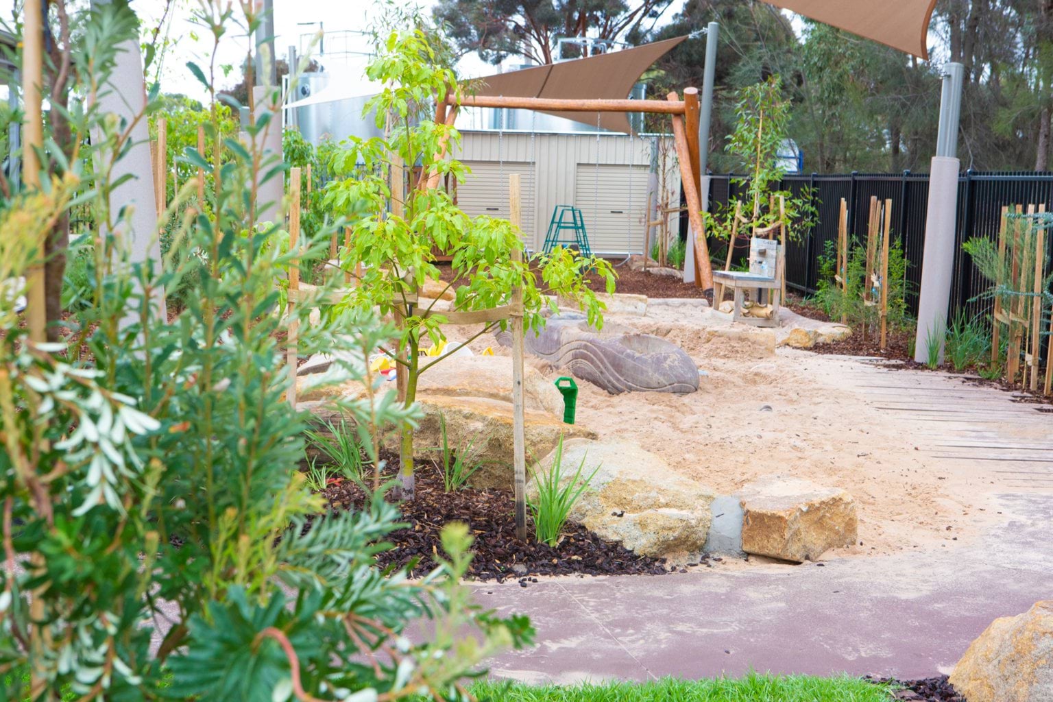Outdoor area at Early Learning Victoria Bani Walup (Murtoa) with foreground greenery, central sandpit and shed in background.