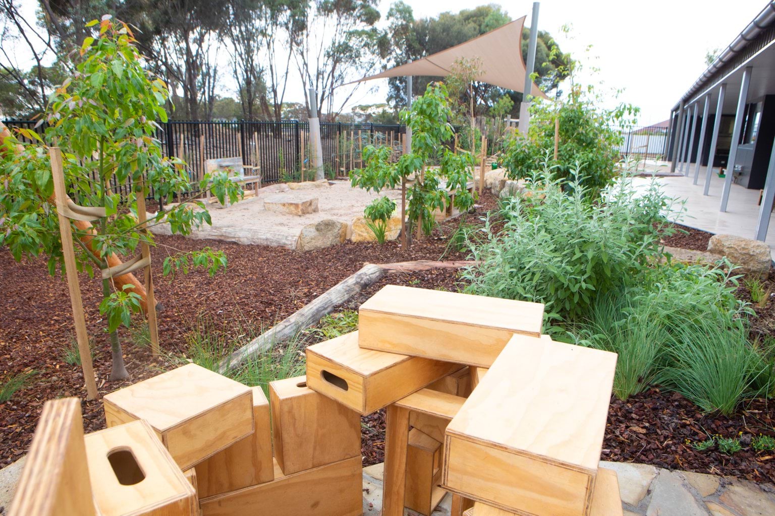 Outdoor play area at Early Learning Victoria Bani Walup (Murtoa) with tanbark, wooden blocks, shade sail and greenery.