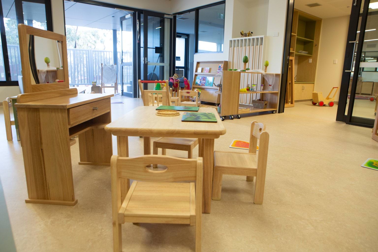 Wide indoor view at Early Learning Victoria Nyernilang Lar (Eaglehawk North) showing wooden tables, chairs, various toys and door leading outside.